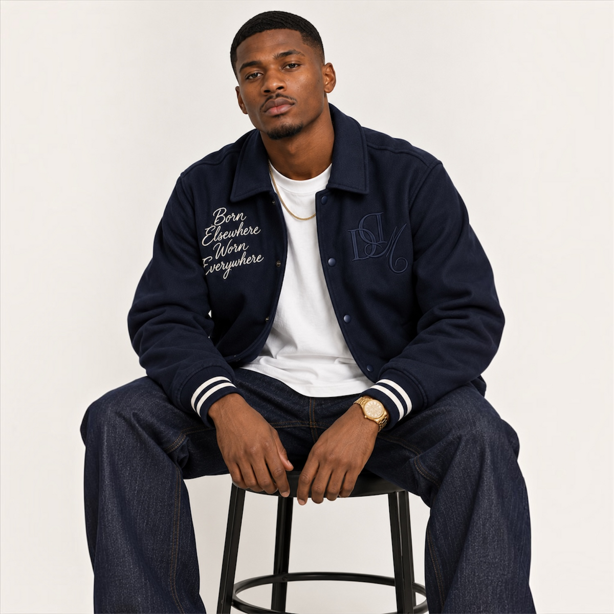 Seated model wearing DonDeMarco navy varsity wool jacket