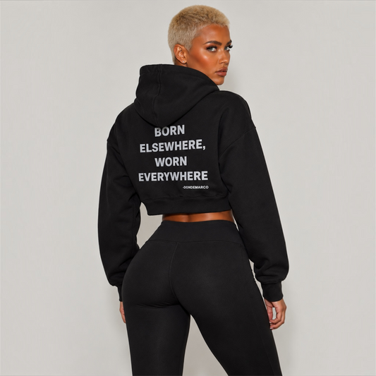 Model wearing the black DonDeMarco women’s Passport cropped hoodie, back view showing Born Elsewhere Worn Everywhere lettering
